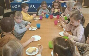 Zdjęcie przedstawia dzieci siedzące przy stoliku jedzących babkę.