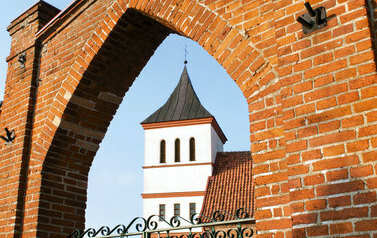 Zdjęcie przedstawia widok na Kości&oacute;ł przez bramę w Straszewie